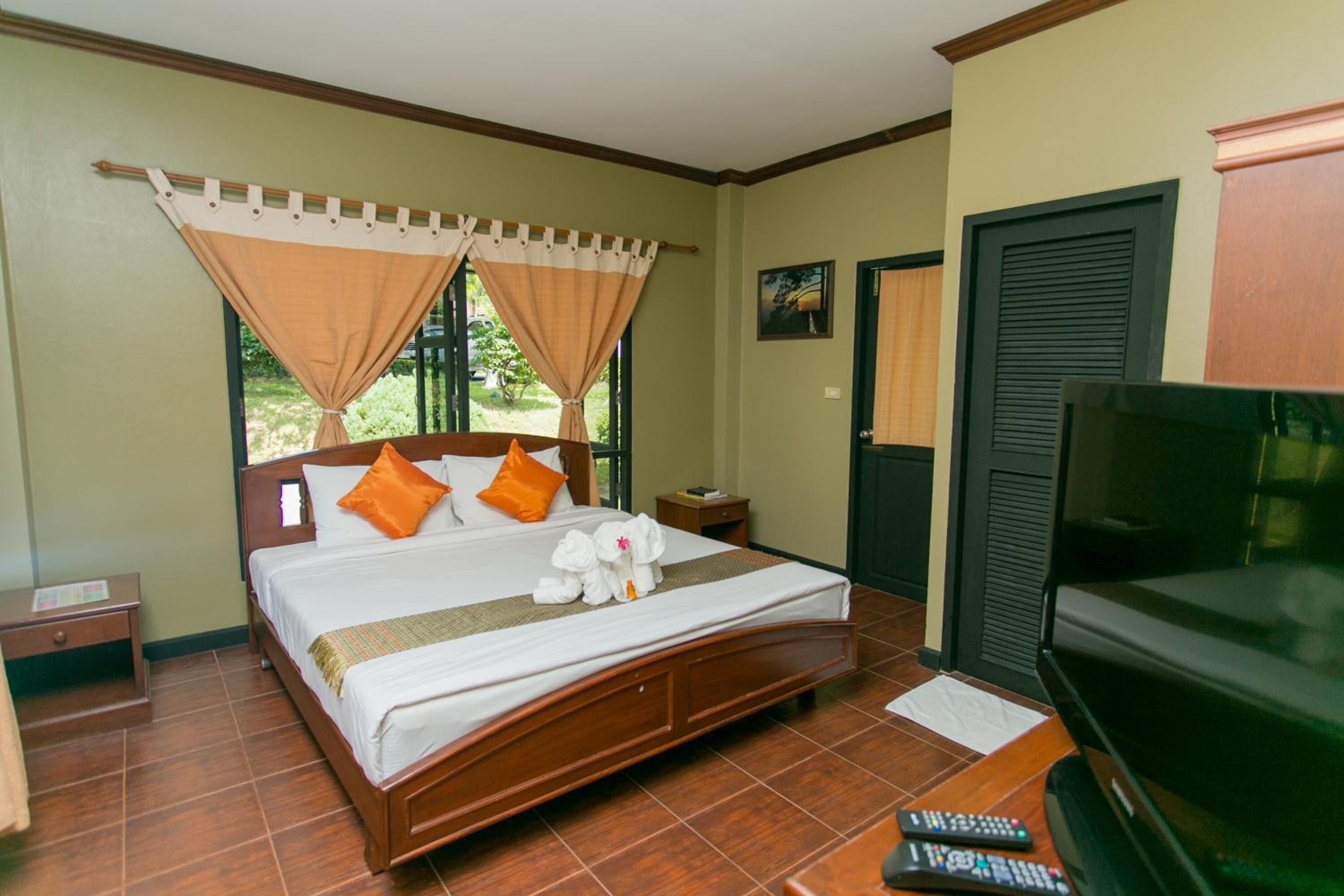 Hotelkamer met een houten bed, twee kussens, een nachtkastje, een televisie en een raam met gordijnen.