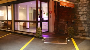 Entrada de hotel con fachada de vidrio, pared de piedra y toldo naranja con el nombre 'ENTRATA RINGANG'.