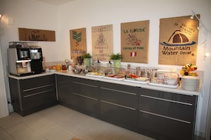 A kitchen with a coffee station, buffet setup, and decorative coffee-themed wall art. - Hotel Garni Morettina (Brissago)