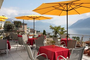 Terraza exterior con mesas y sillas, sombrillas amarillas y vistas a un lago y montañas.