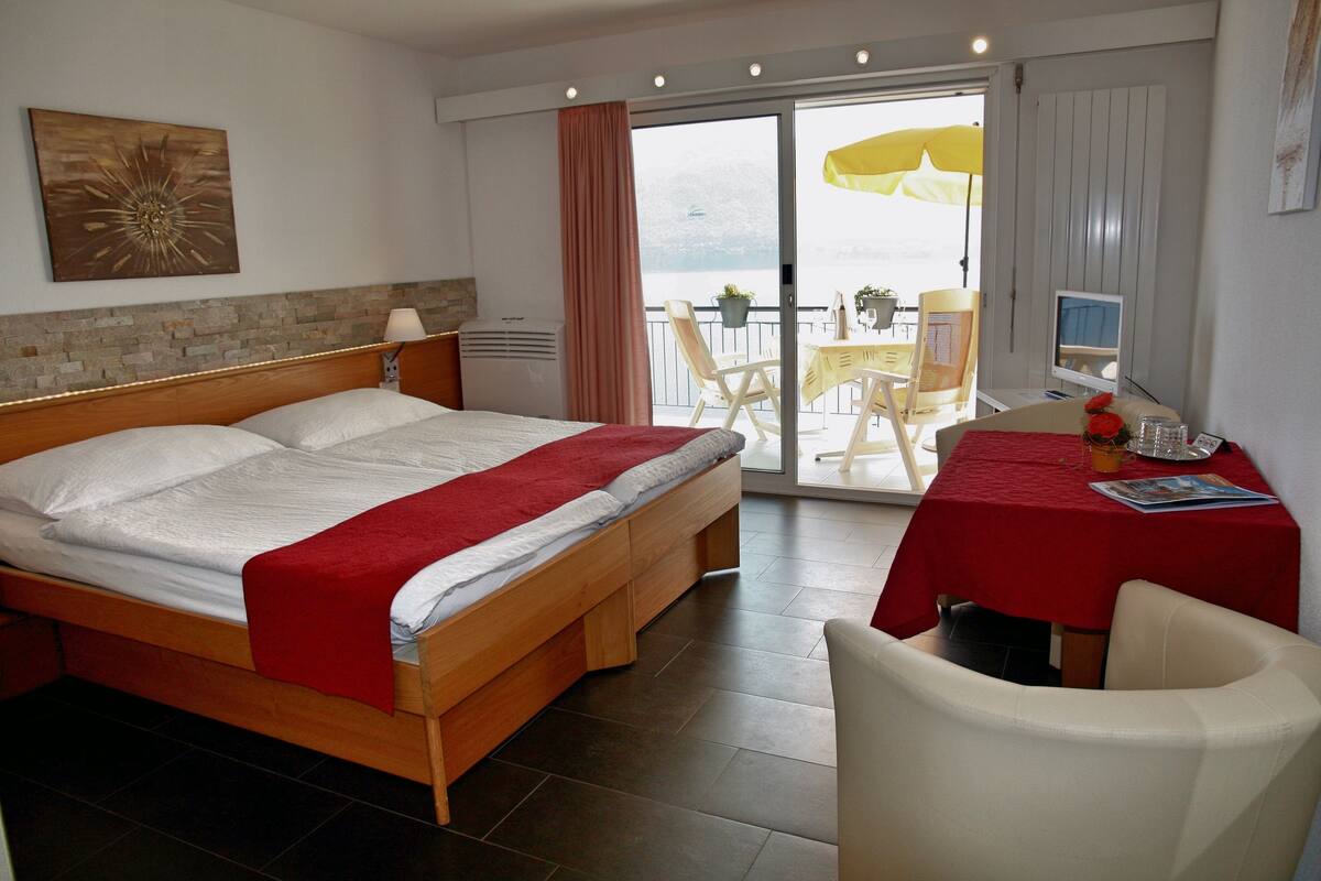 Hotelkamer met een bed, een bureau met een computer, een stoel en een balkon met een tafel en stoelen.