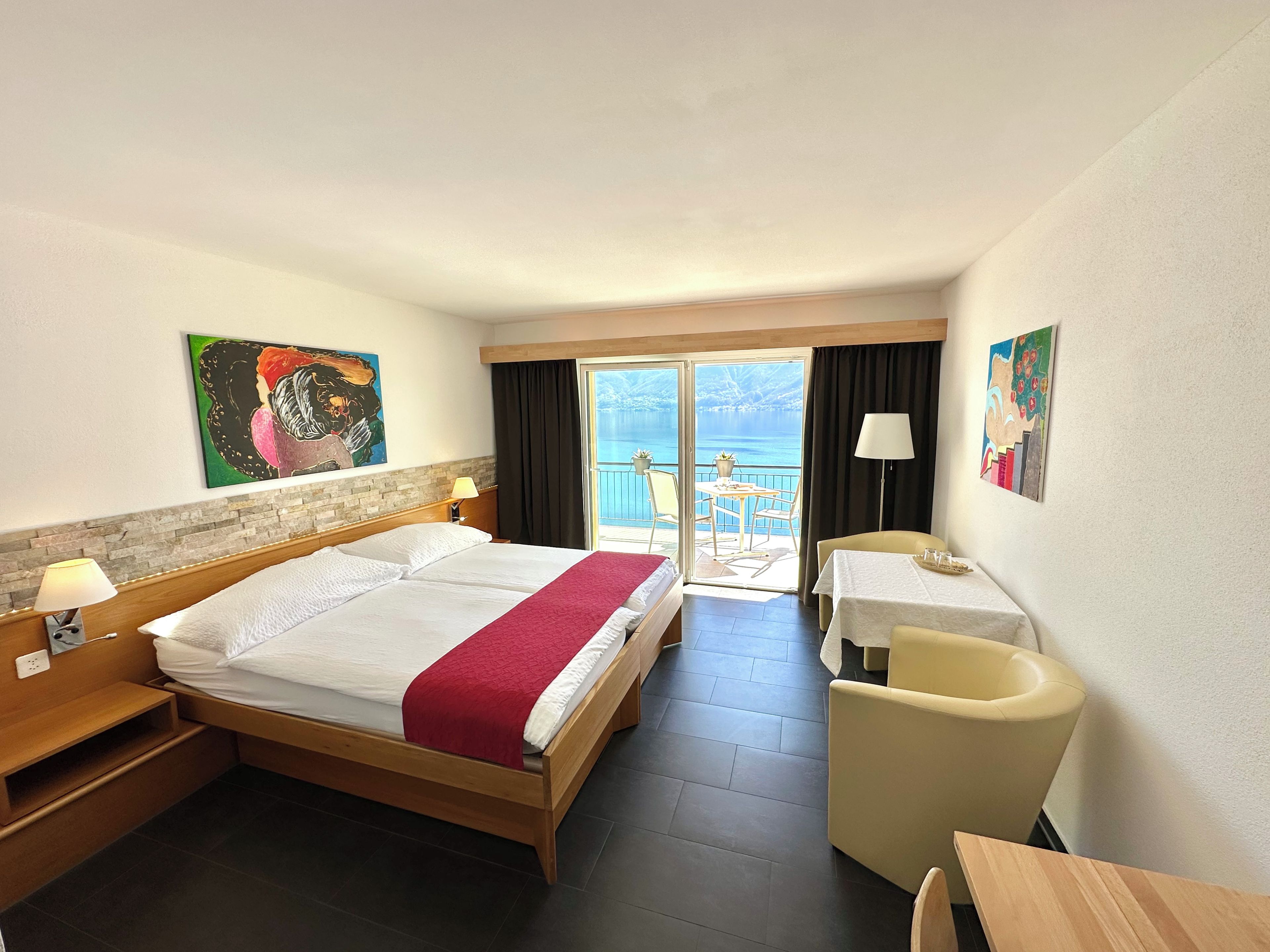 Een hotelkamer met een bed, bureau, stoel, tafel en een balkon met uitzicht op zee.
