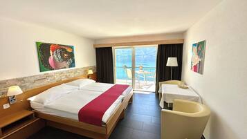 Een hotelkamer met een bed, bureau, stoel, tafel en een balkon met uitzicht op zee.
