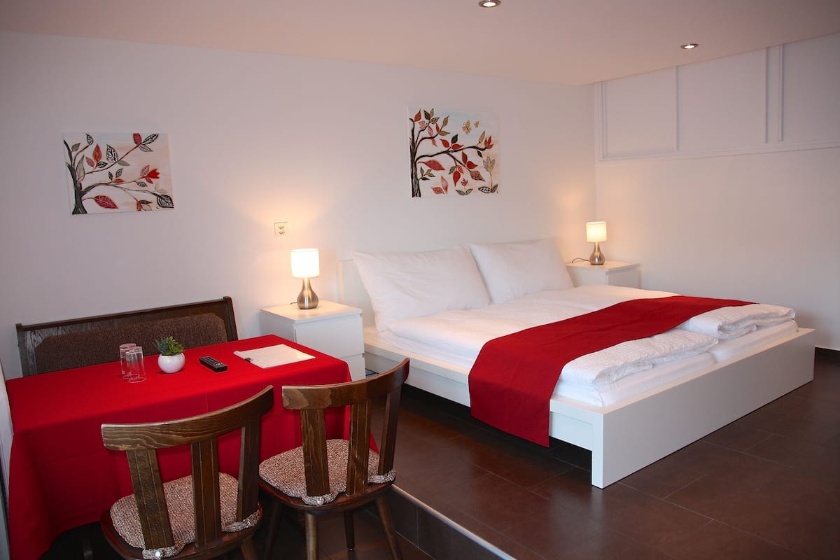Een slaapkamer met een bed, nachtkastjes, een bureau met stoelen en twee decoratieve wandschilderingen.