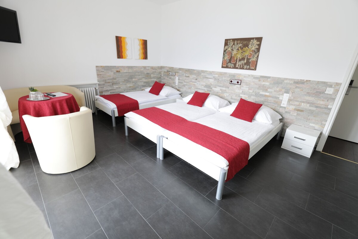 Habitación de hotel con dos camas, una mesita redonda pequeña, una silla y un radiador.