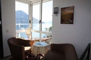 Habitación con vistas a un lago y montañas, con dos sillones, una mesita con lámpara y un cuadro en la pared.