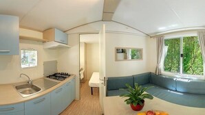 Eine kleine Küche mit Spüle, Herd und Schränken, ein Essbereich mit Tisch und Stühlen sowie eine Sitzecke mit Sofa und Fenster.