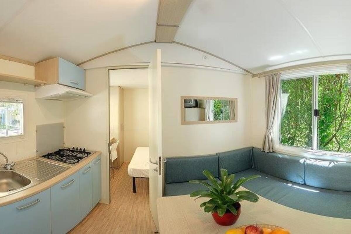 Uma cozinha compacta com pia, fogão e armários, uma área de jantar com mesa e cadeiras, e um espaço de estar com sofá e janela.