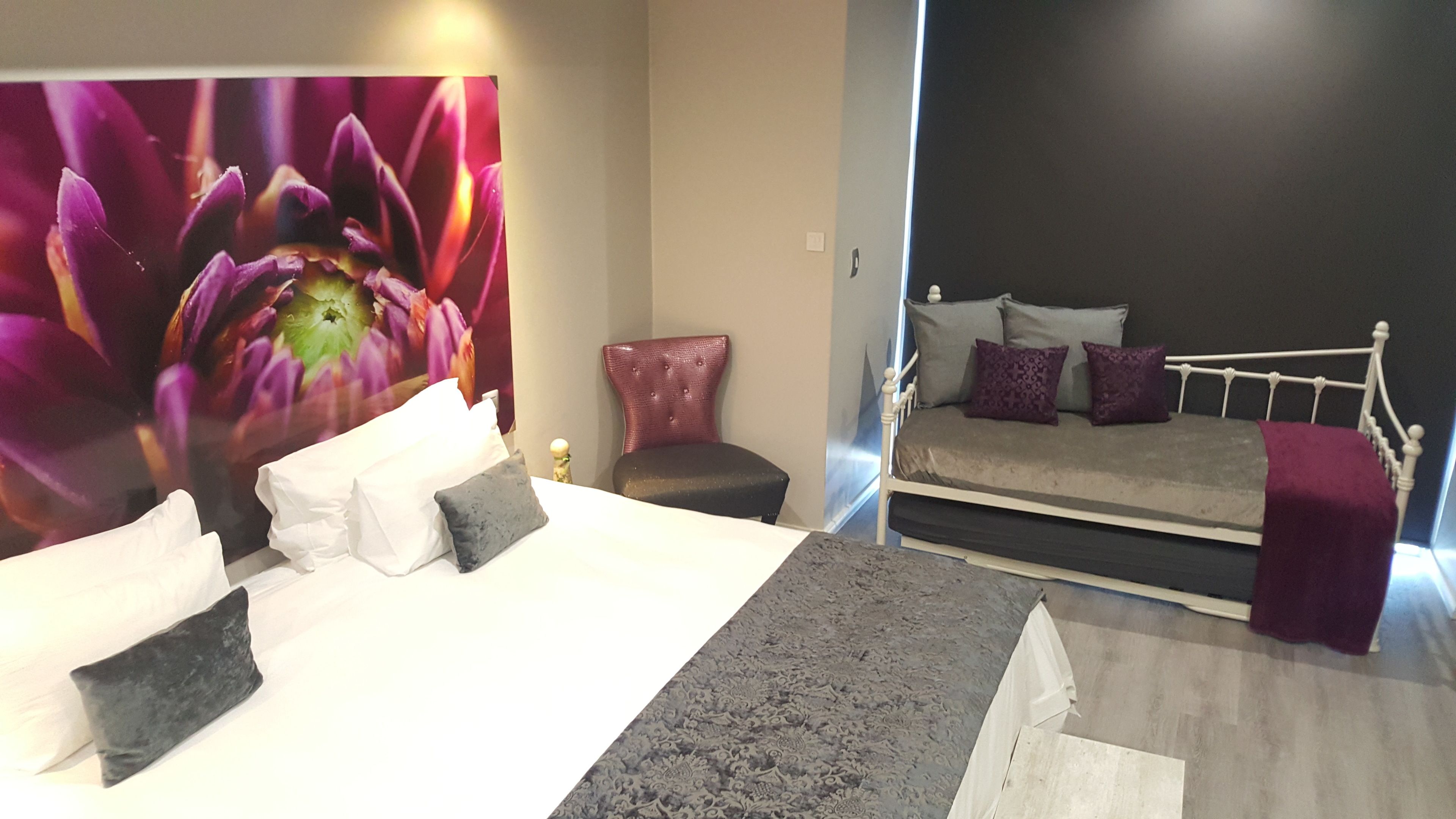 A bedroom with a large floral artwork, a bed with multiple pillows, a chair, and a small table.