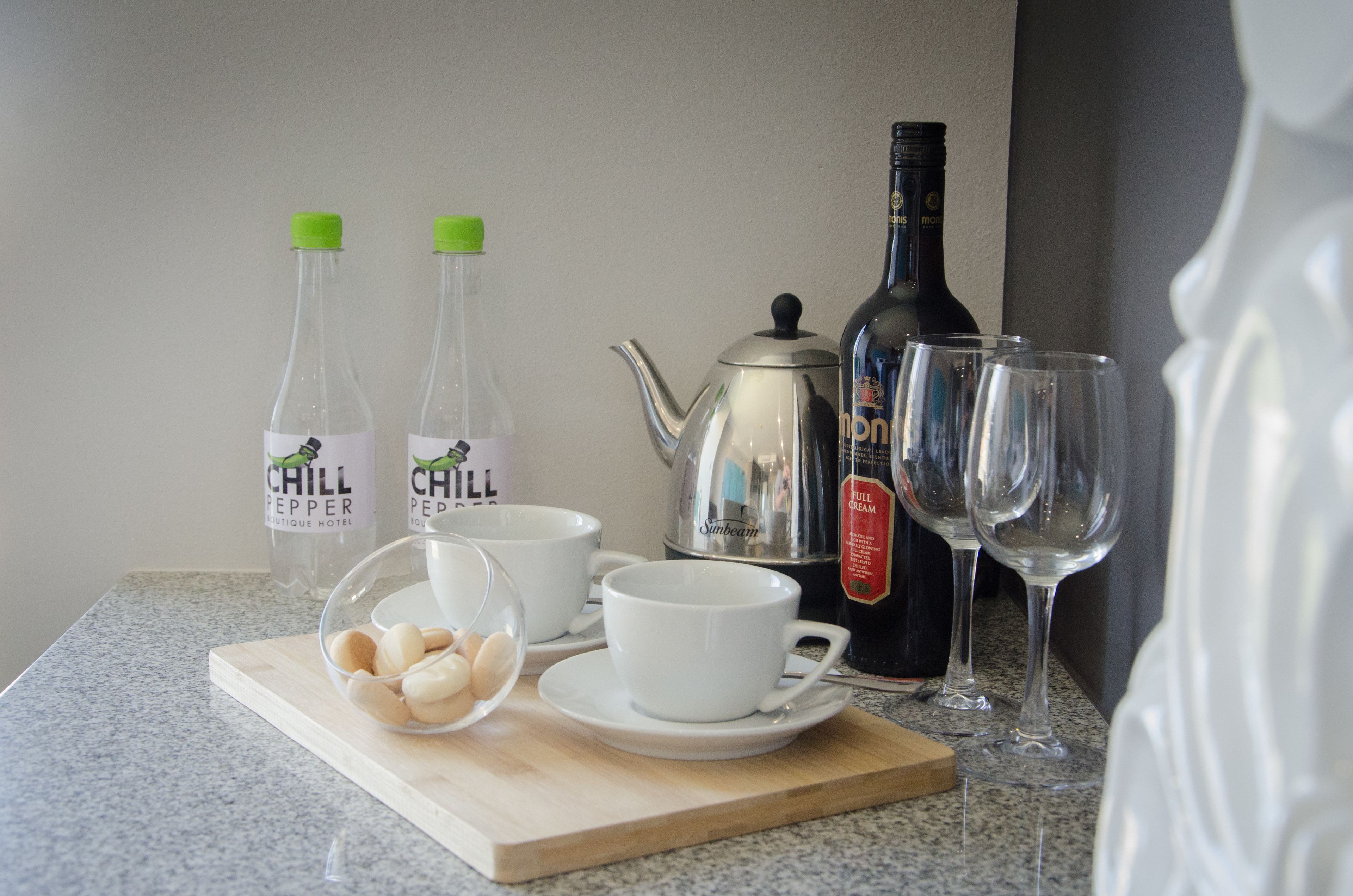 A kitchen counter with two bottles of 'Chill Pepper' tea, a teapot, two white cups, a bowl of eggs, and two wine glasses.