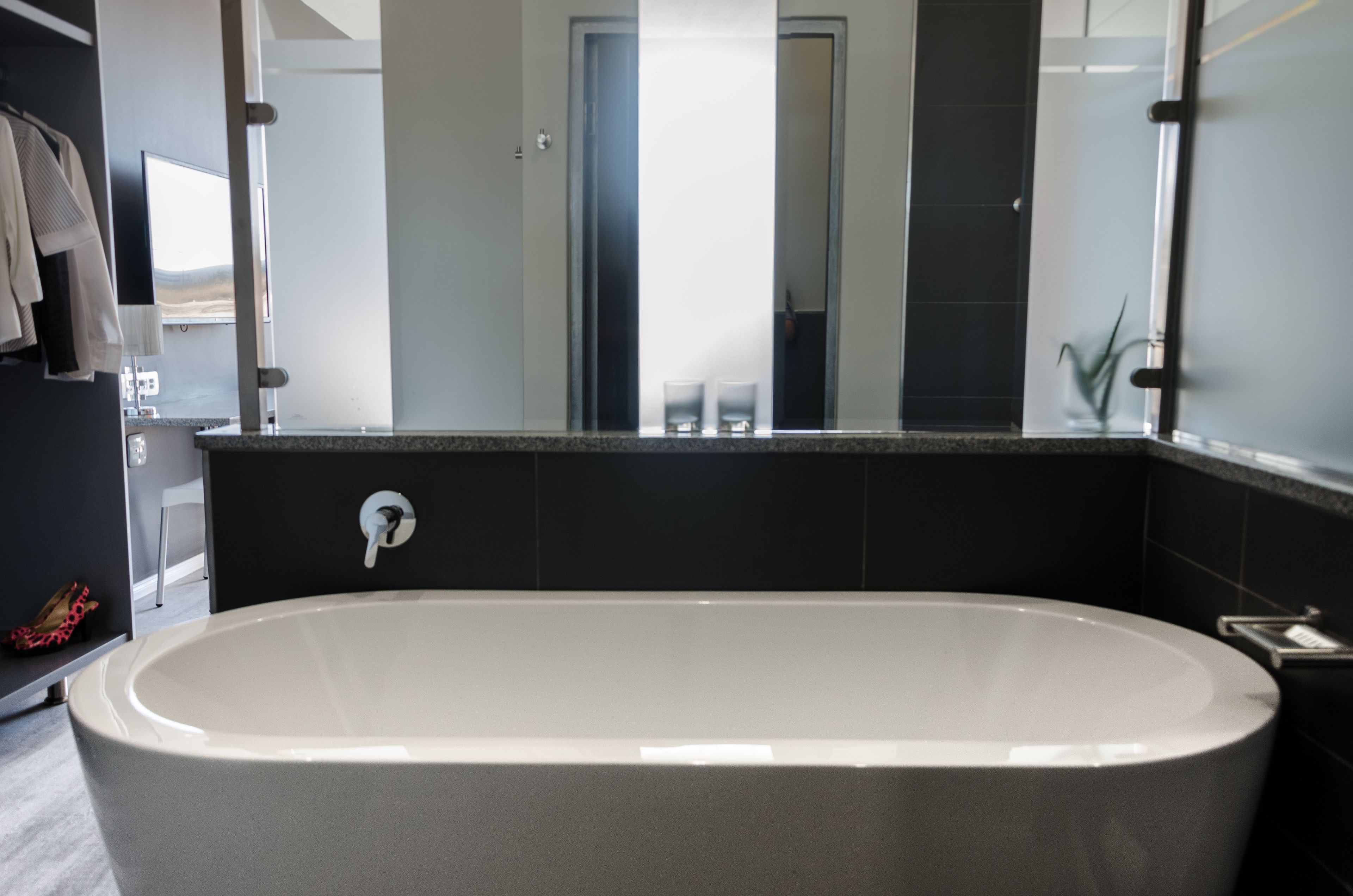 A modern bathroom with a freestanding bathtub, a large mirror, and a dark tiled wall.
