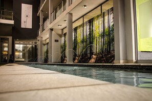 Ein moderner Poolbereich im Innenbereich mit freier Sicht auf den Pool, einem großen Fenster mit einem Waldgemälde und einem klaren, zeitgemäßen Design.