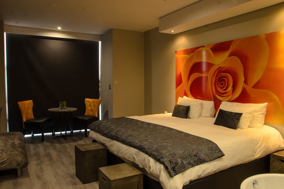 Een moderne slaapkamer met een groot bed, twee stoelen, een kleine tafel en een groot kunstwerk met bloemen aan de muur.