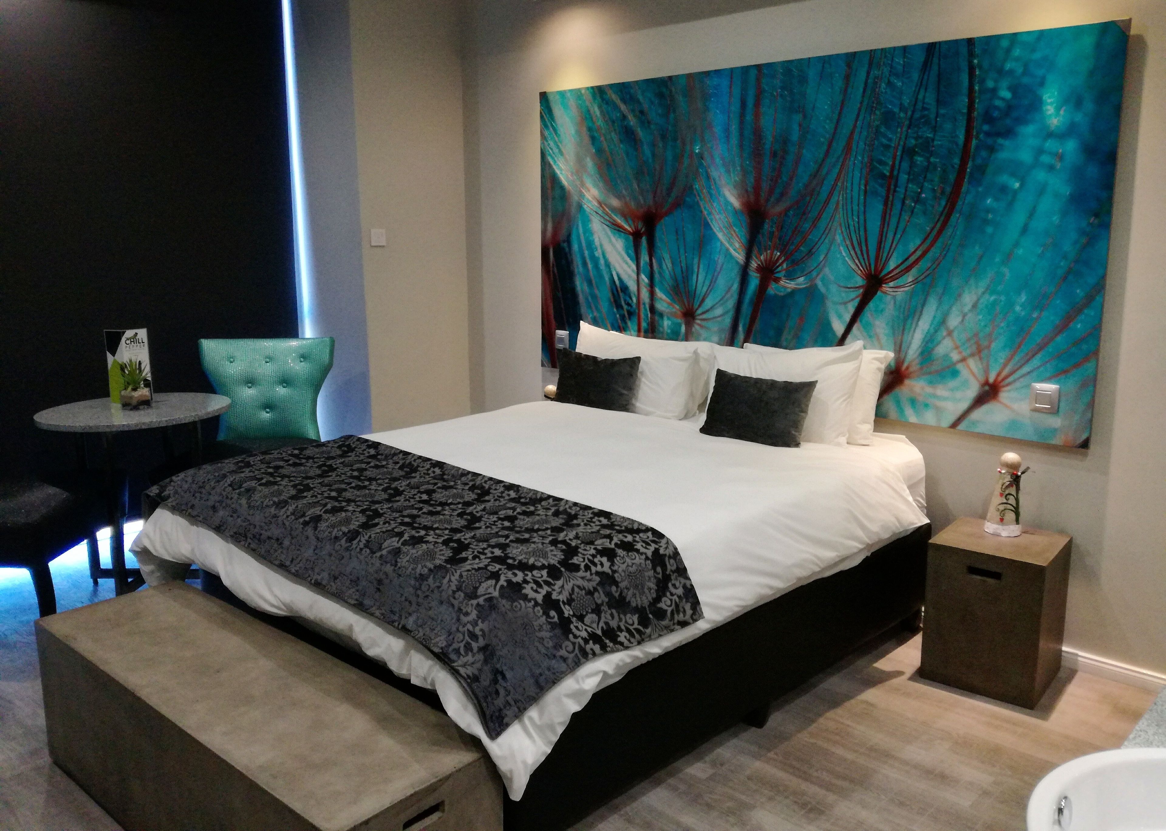 A modern bedroom with a large bed, a small round table, a bench, and a painting on the wall.