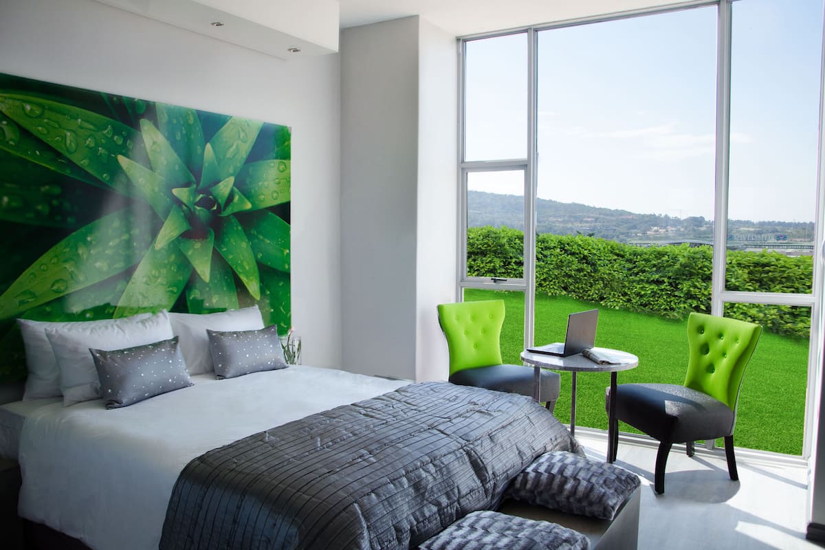 Een moderne slaapkamer met een groot bed, groene stoelen en een laptop op een bijzettafeltje.