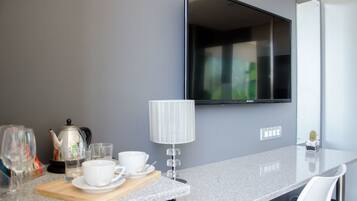 A modern kitchen with a granite countertop, a kettle, cups, and a small cactus on the counter.