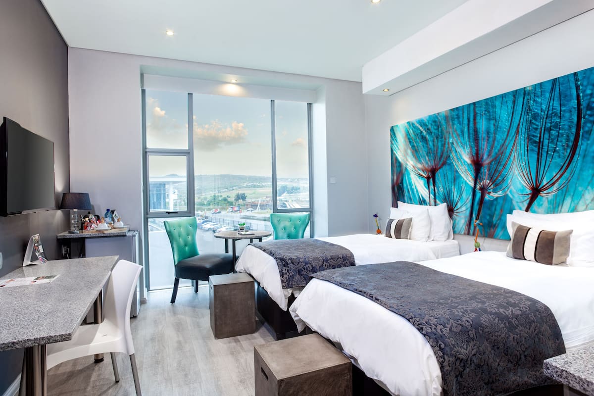 Een hotelkamer met twee bedden, een bureau en een groot raam met uitzicht op de stad.
