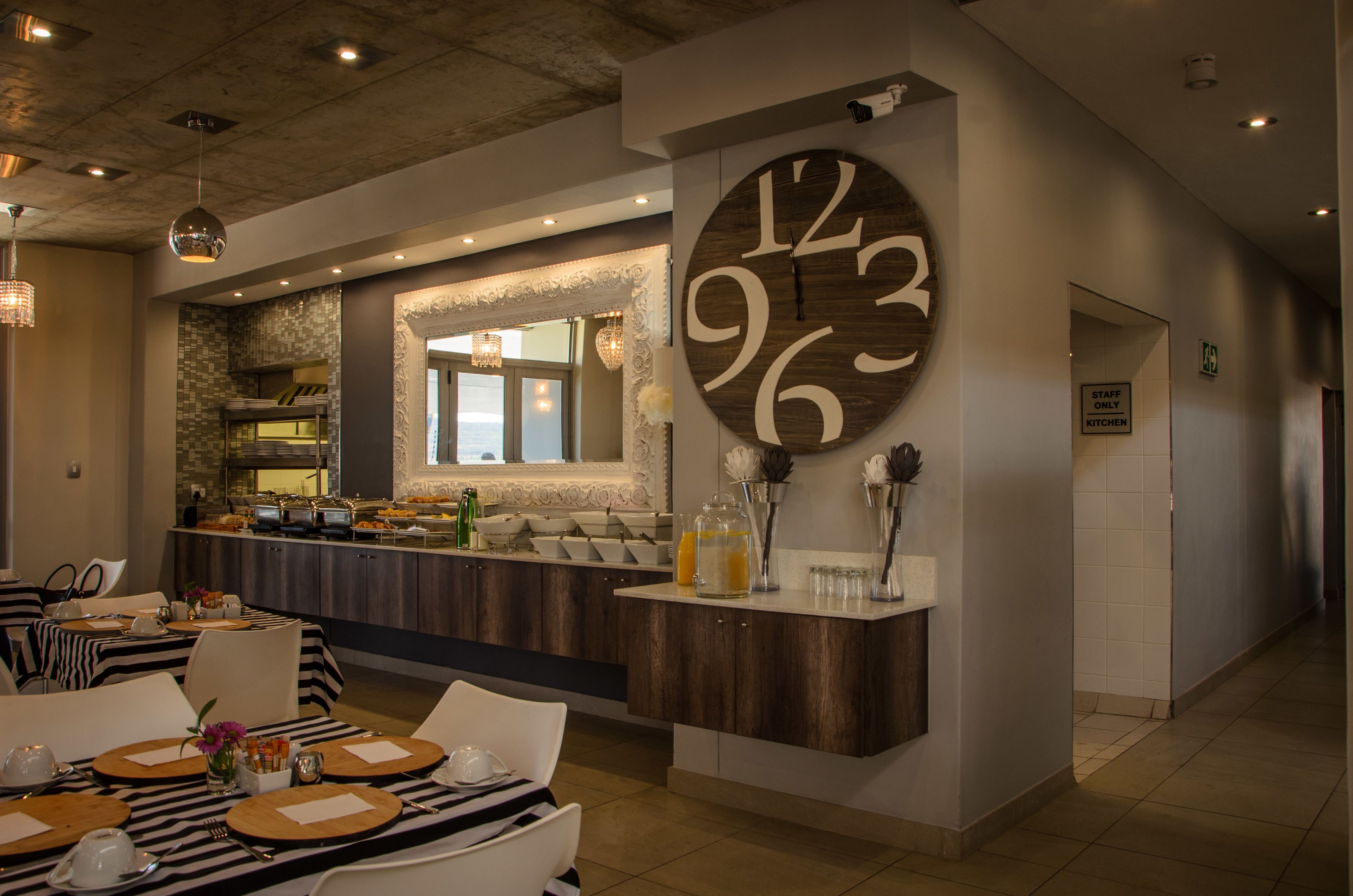 A hotel lobby with a large wall clock, a buffet area, and a seating area with tables set for dining.