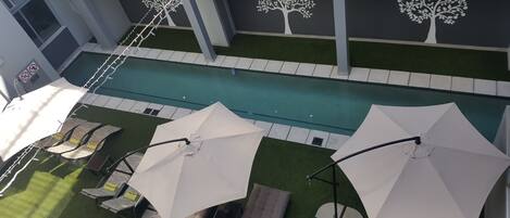 Un espace extérieur avec piscine, comprenant des chaises longues et des parasols, entouré de gazon synthétique et bordé d’une piscine dont le pourtour est recouvert de carreaux.
