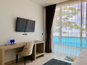 A hotel room with a bed, a desk with a chair, a television, and a view of a pool. - Sikhara Plago Resort (Chonburi)