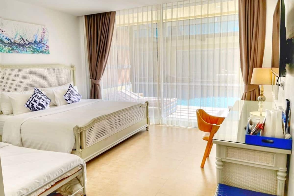 Habitación de hotel con cama, escritorio, silla, televisor y vista a una piscina.