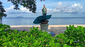 Una estatua de una figura con vestido tropical sobre un pedestal, junto al mar.
