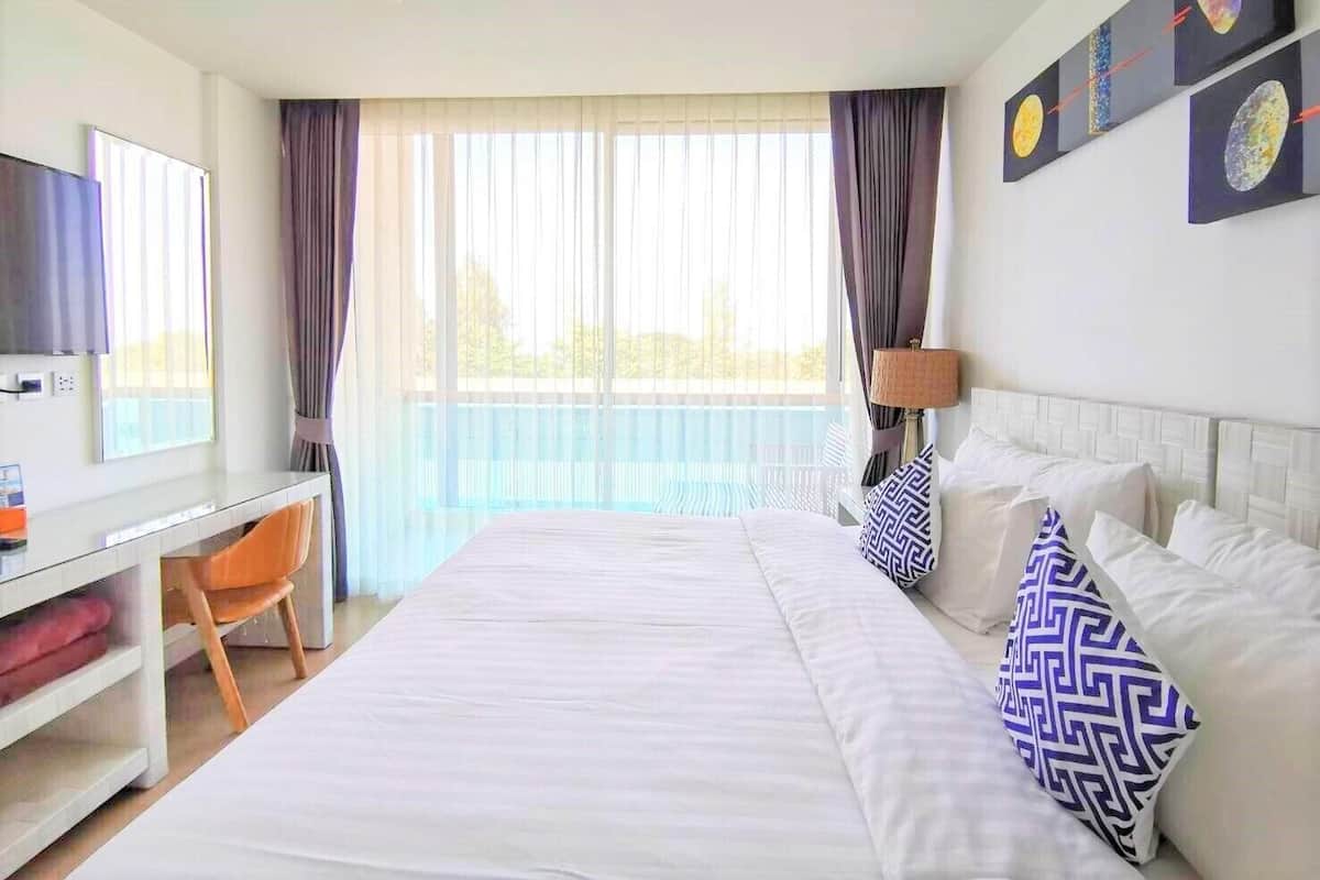 Habitación de hotel con cama, escritorio, silla, televisor y balcón con cortinas.