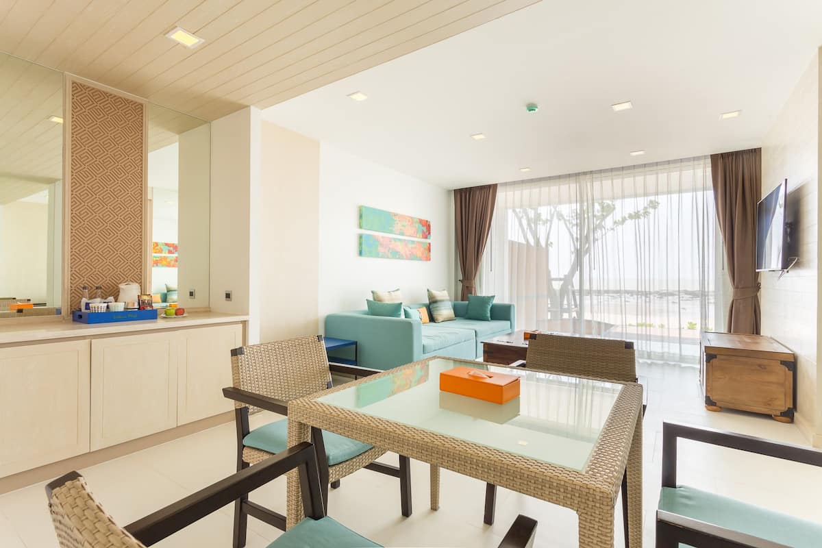 Una sala de estar moderna con una mesa de comedor de vidrio, sillas de mimbre, un sofá y un televisor montado en la pared.