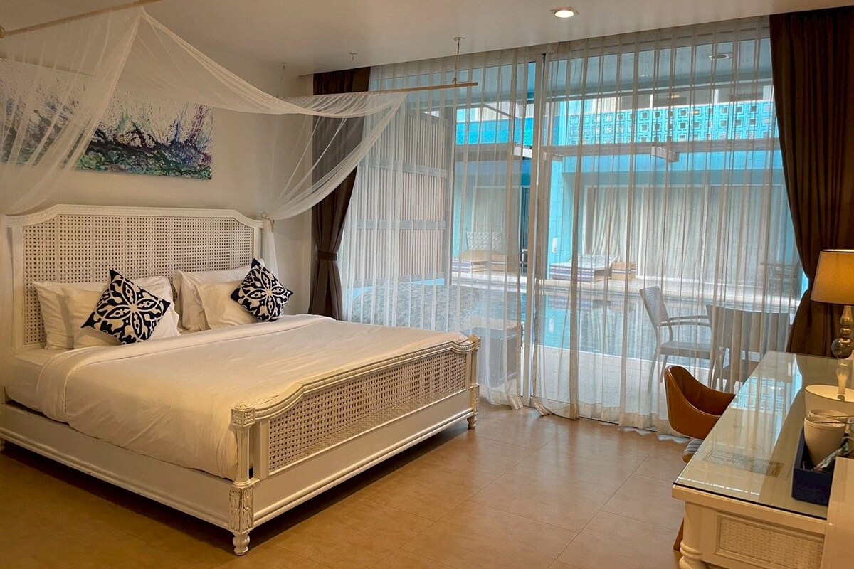 A hotel room with a four-poster bed, a balcony with a view, and a desk with a lamp.