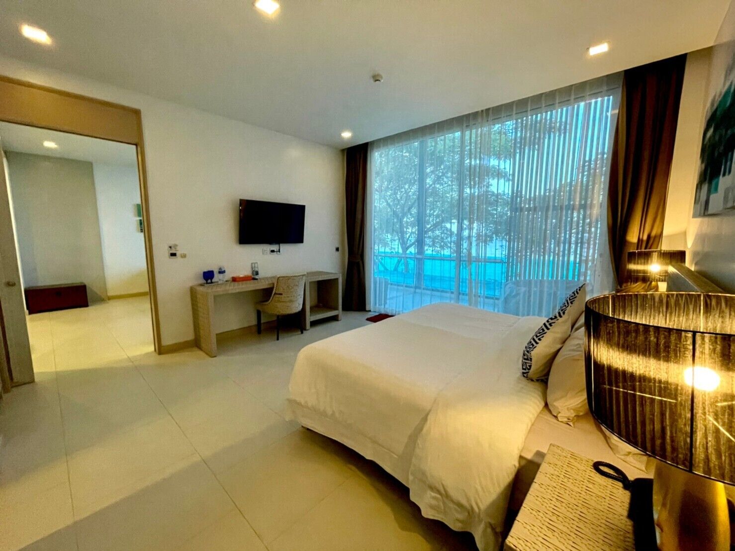 A hotel room with a bed, a desk, a TV, and a large window with curtains.
