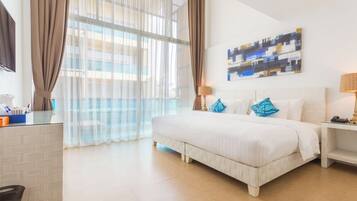 A hotel room with a large bed, a desk, a chair, and a window with curtains.