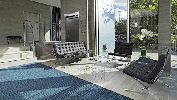 Um lobby moderno com um sofá de couro preto, uma mesa de centro de vidro e um tapete azul.