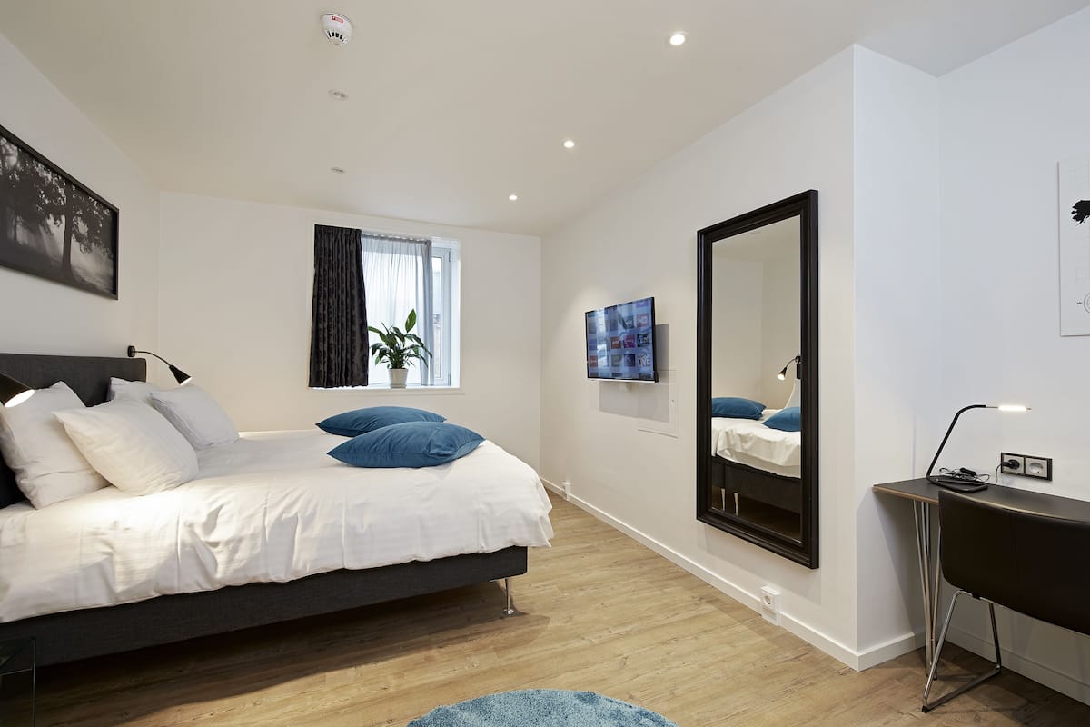 Quarto moderno com uma cama grande, uma escrivaninha, um espelho e uma janela com cortinas.