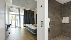 Quarto moderno com uma cama grande, escrivaninha com cadeiras e área de chuveiro com paredes em azulejo.
