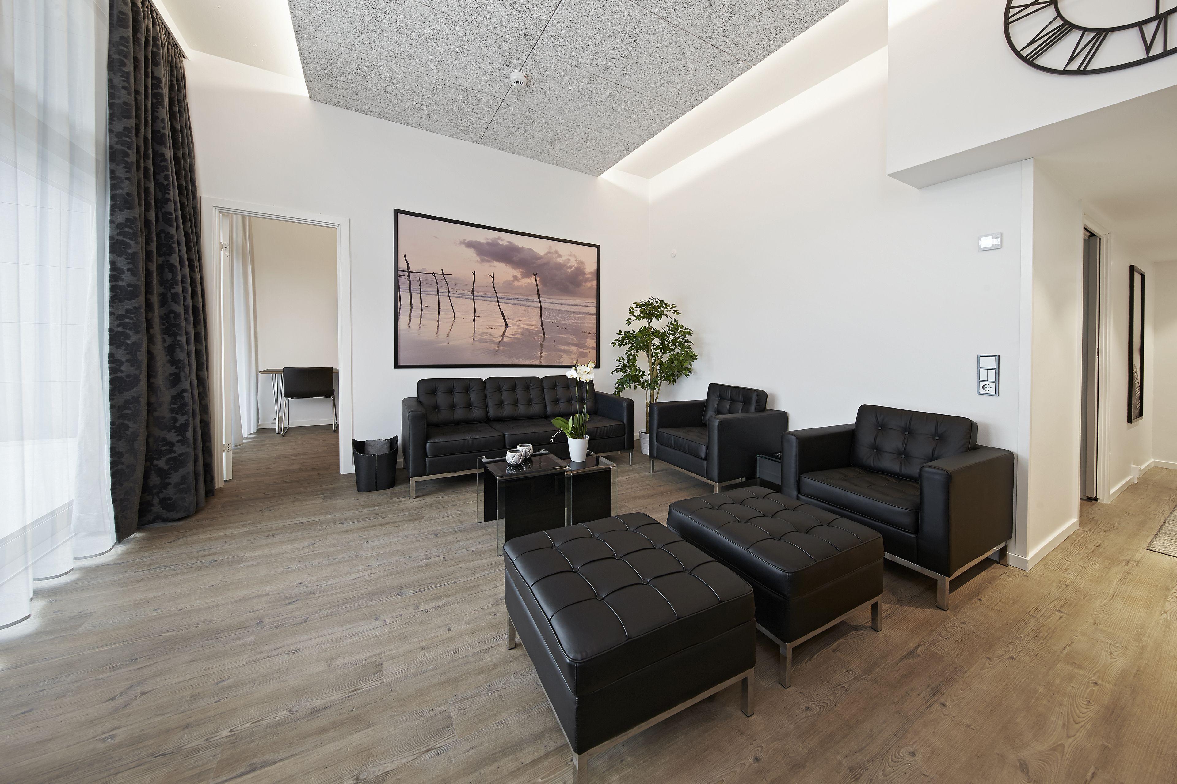 Una sala de estar moderna con un cuadro grande, sofás de cuero negro y suelo de madera.
