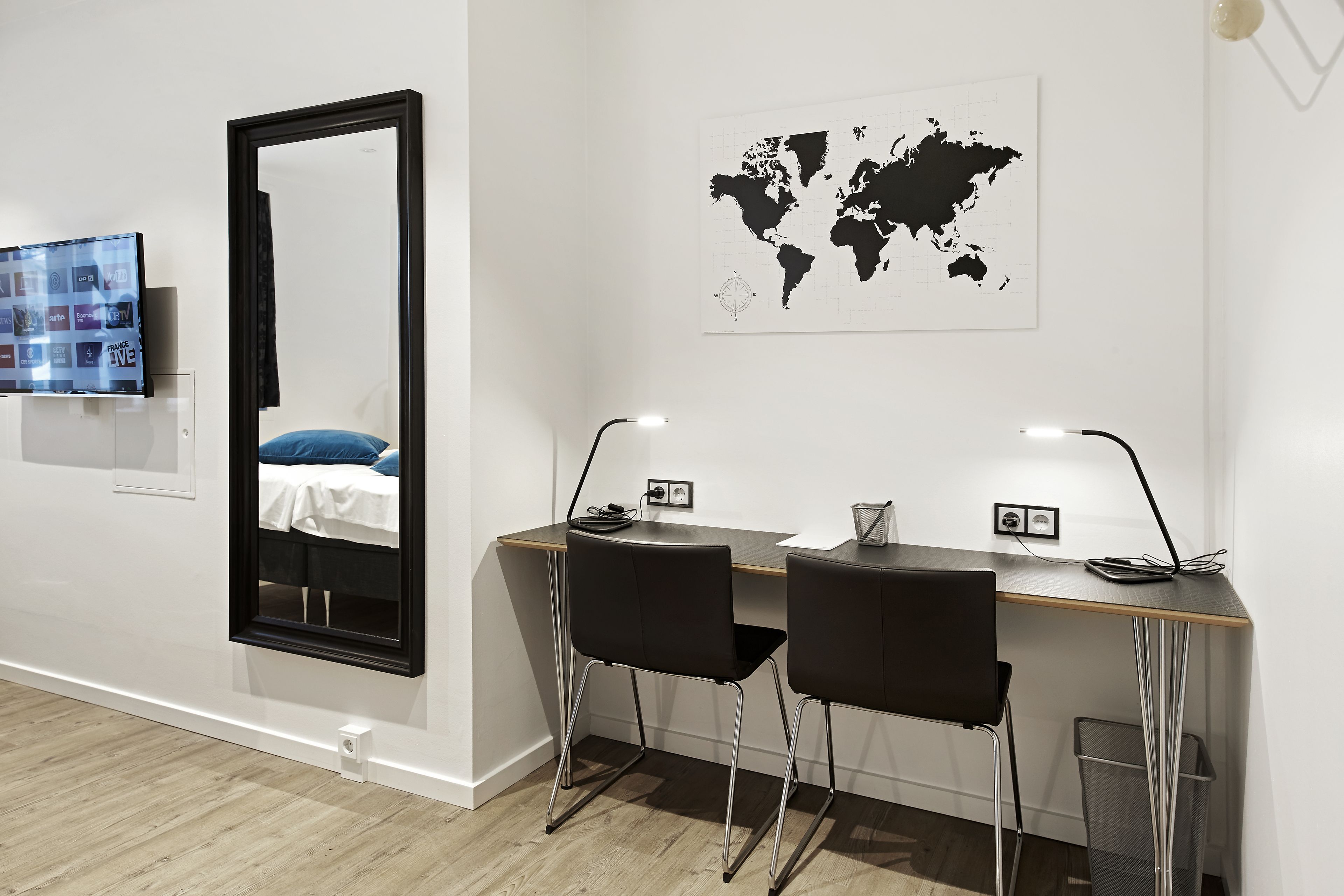 A modern room with a large mirror, two black chairs, a wooden desk, and a world map on the wall.
