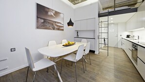 Uma cozinha moderna com armários brancos, um espaço de jantar com mesa e cadeiras brancas, e uma escadaria que leva a um andar superior.