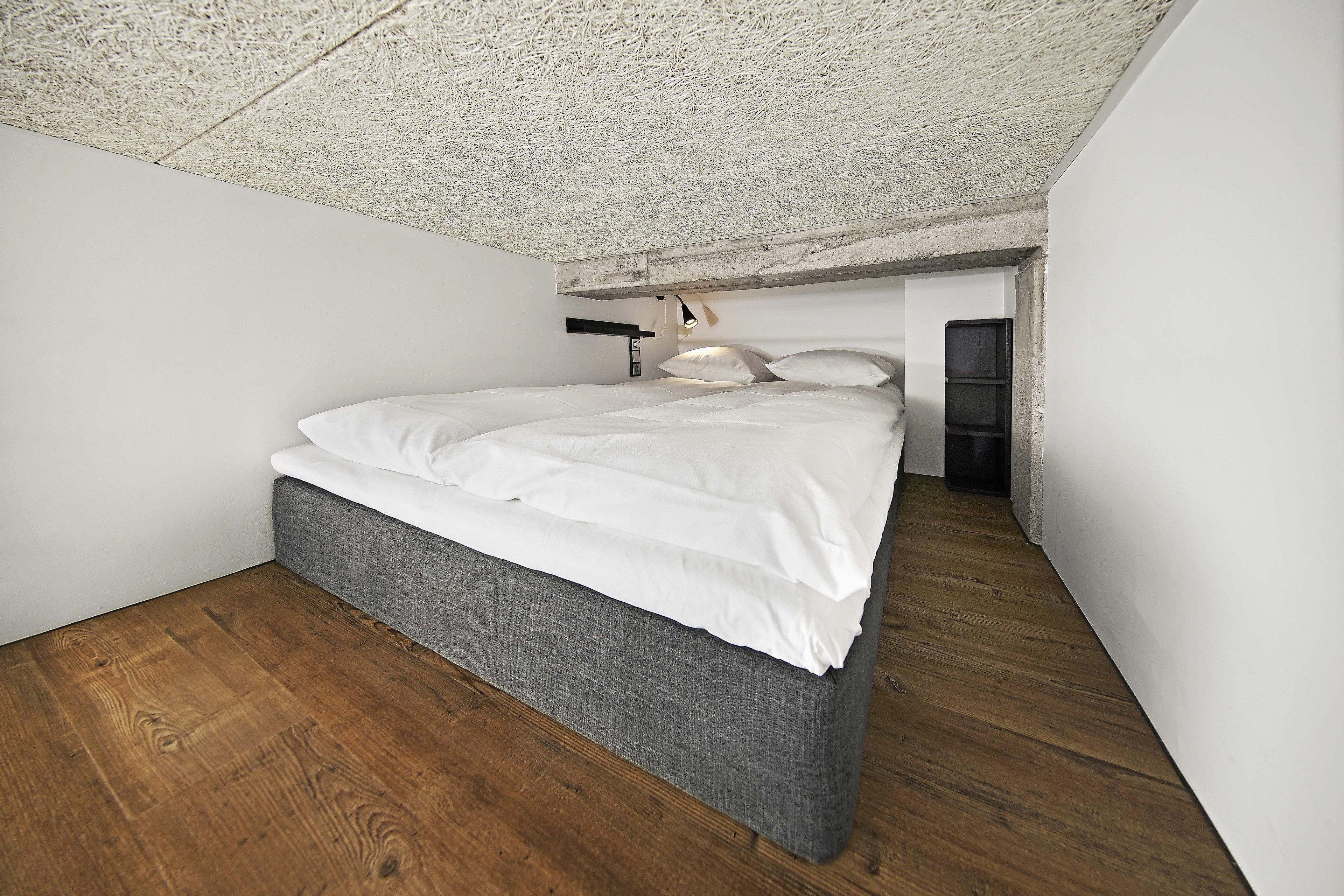 Un dormitorio con cama, suelo de madera y techo texturizado.