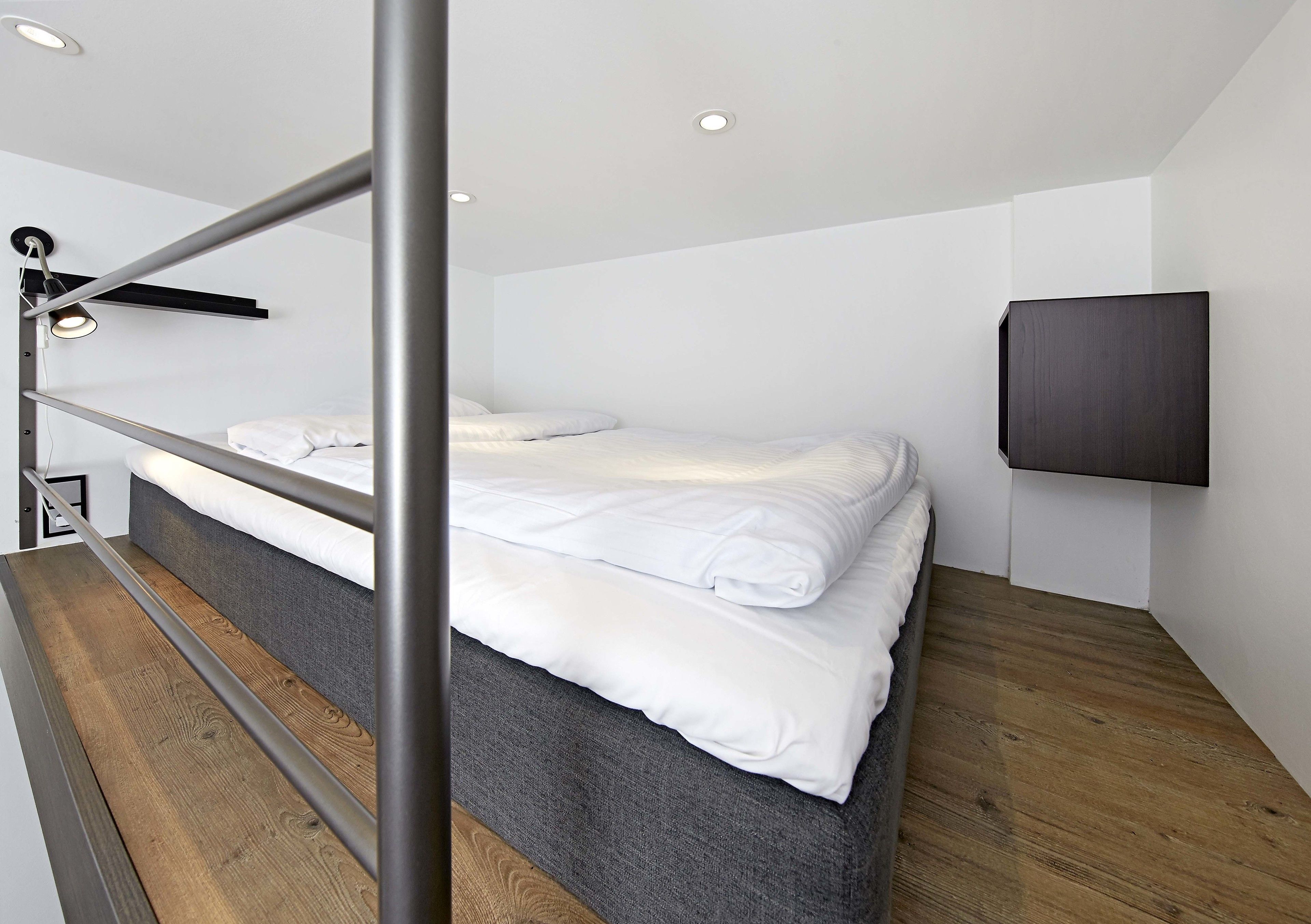 A modern hotel room with a bunk bed, a flat-screen TV mounted on the wall, and a wooden floor.