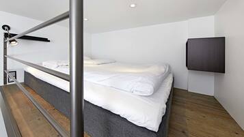 A modern hotel room with a bunk bed, a flat-screen TV mounted on the wall, and a wooden floor.