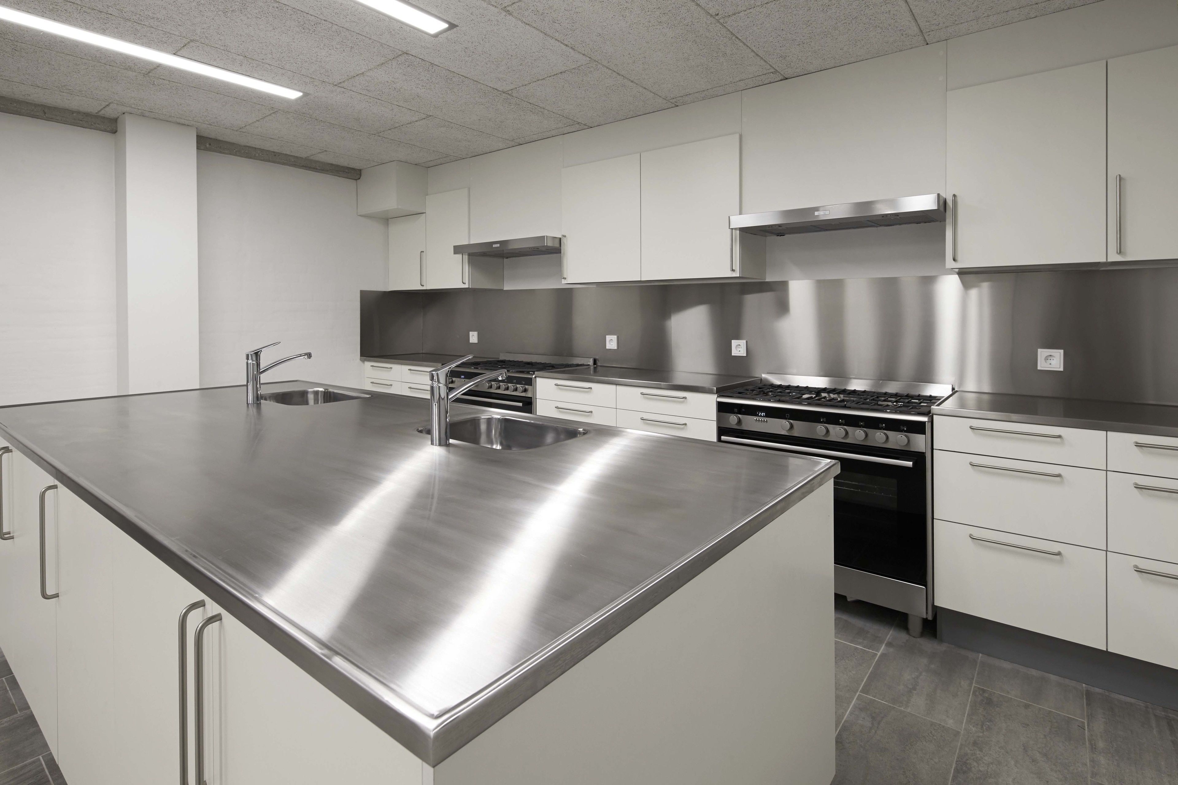 A modern kitchen with stainless steel appliances, white cabinetry, and a large island with a sink.