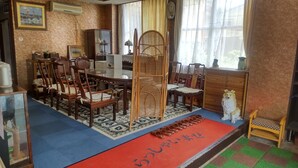 Une pièce de style japonais traditionnel, avec un sol recouvert de tatamis, une table basse entourée de chaises, un paravent décoratif en bois et un tapis rouge orné de caractères japonais.