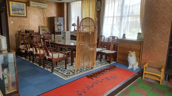 Una habitación tradicional japonesa con suelo de esteras de tatami, una mesa baja con sillas, un biombo decorativo de madera y una estera roja con caracteres japoneses.
