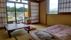 Una habitación japonesa tradicional con suelo de tatami, un futón, una mesita con un control remoto y una puerta corredera estilo shoji.