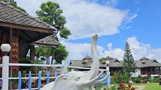 A white elephant statue in a garden with traditional buildings in the background. - Pai River Villa (Pai)