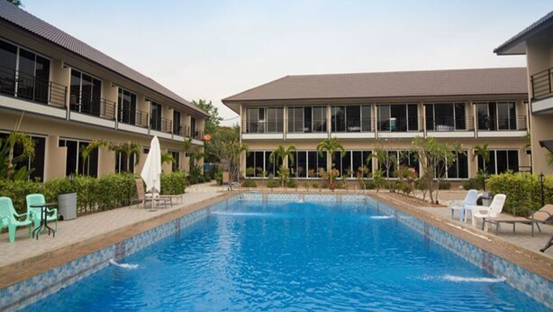 A swimming pool with lounge chairs and umbrellas, surrounded by a building with large windows and a flat roof. - Sky Resort (Kanchanaburi)
