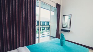 A hotel room with a bed, a window with curtains, a balcony view, and a small table with a mirror. - Sky Resort (Kanchanaburi)