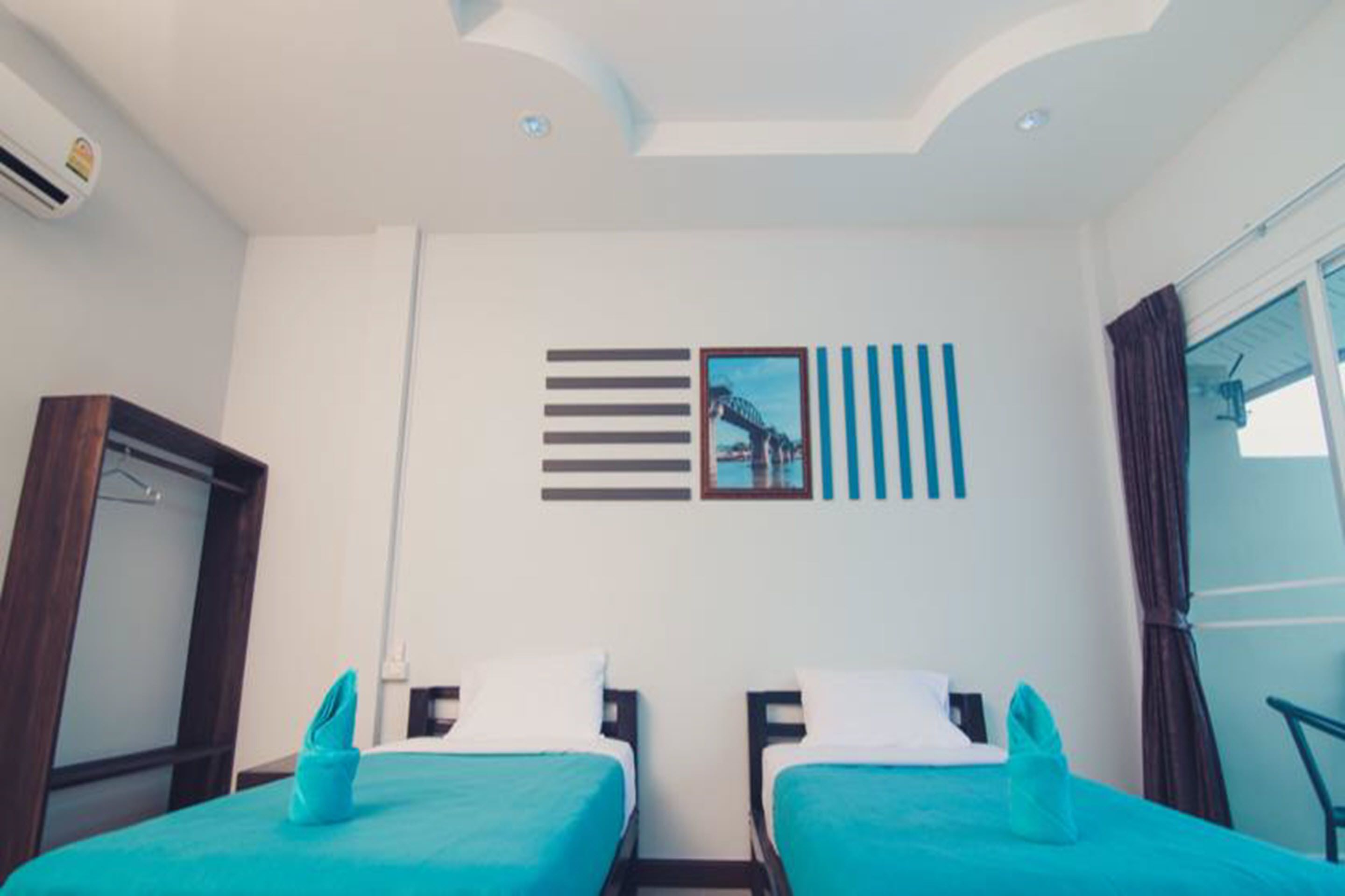 A hotel room with two beds, a wardrobe, a window with curtains, and a wall with a picture and decorative lines.