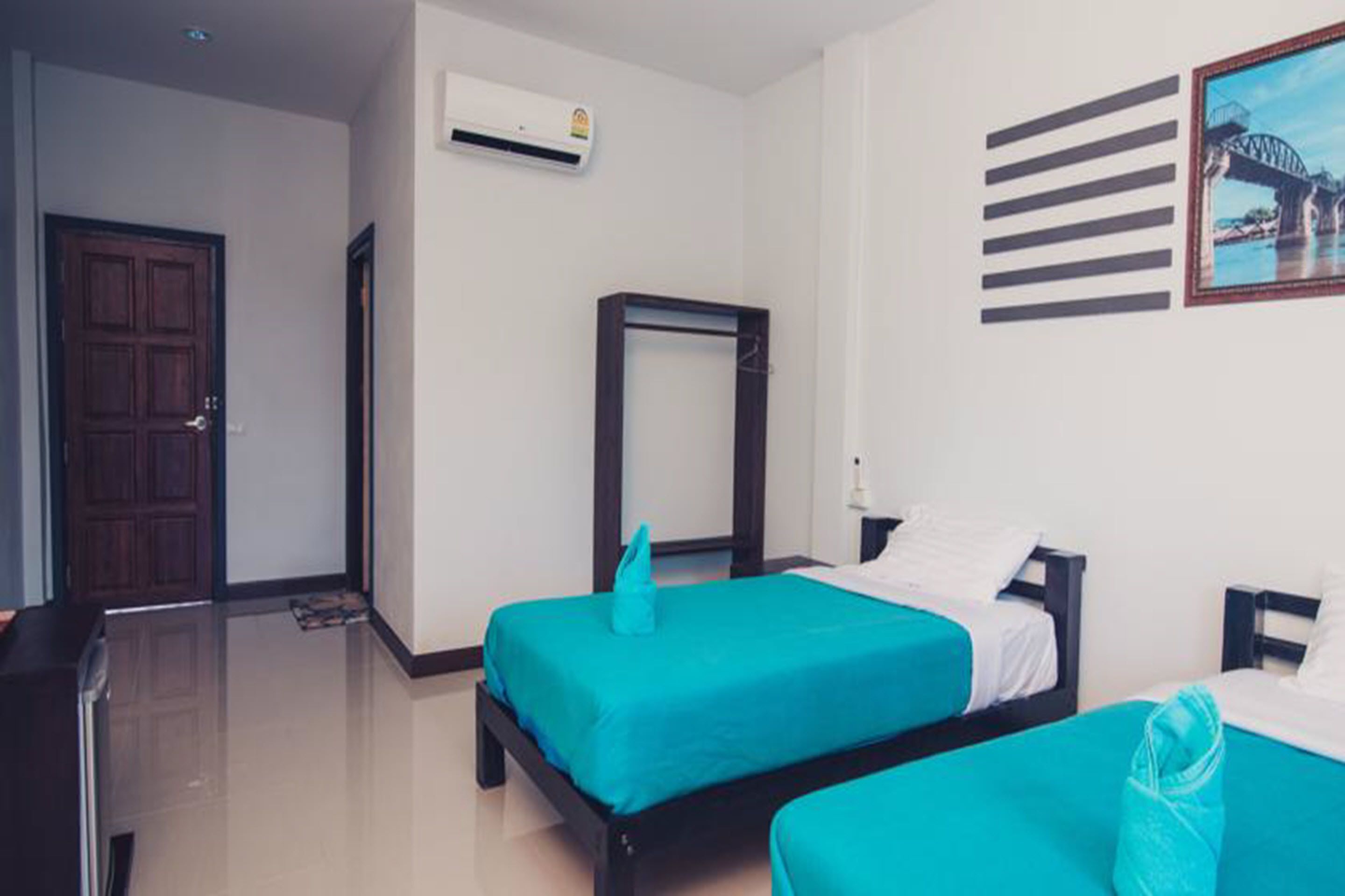A hotel room with two beds, a wooden door, an air conditioning unit, and a framed picture on the wall.