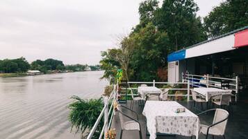 Un restaurante junto al río con terraza al aire libre y vistas al agua.